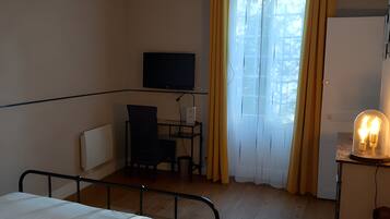 Une chambre d’hôtel avec un lit, un bureau, une chaise, une télévision et une fenêtre avec des rideaux.