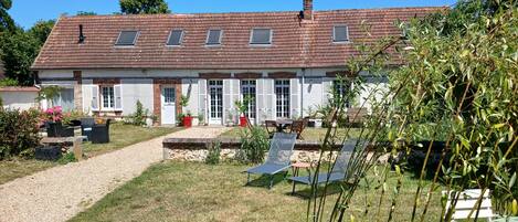 A two-story house with a tiled roof, a gravel driveway, and a garden with potted plants and outdoor furniture.