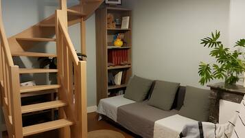 Een kamer met een houten trap, een bank, een boekenkast en een hanglamp.