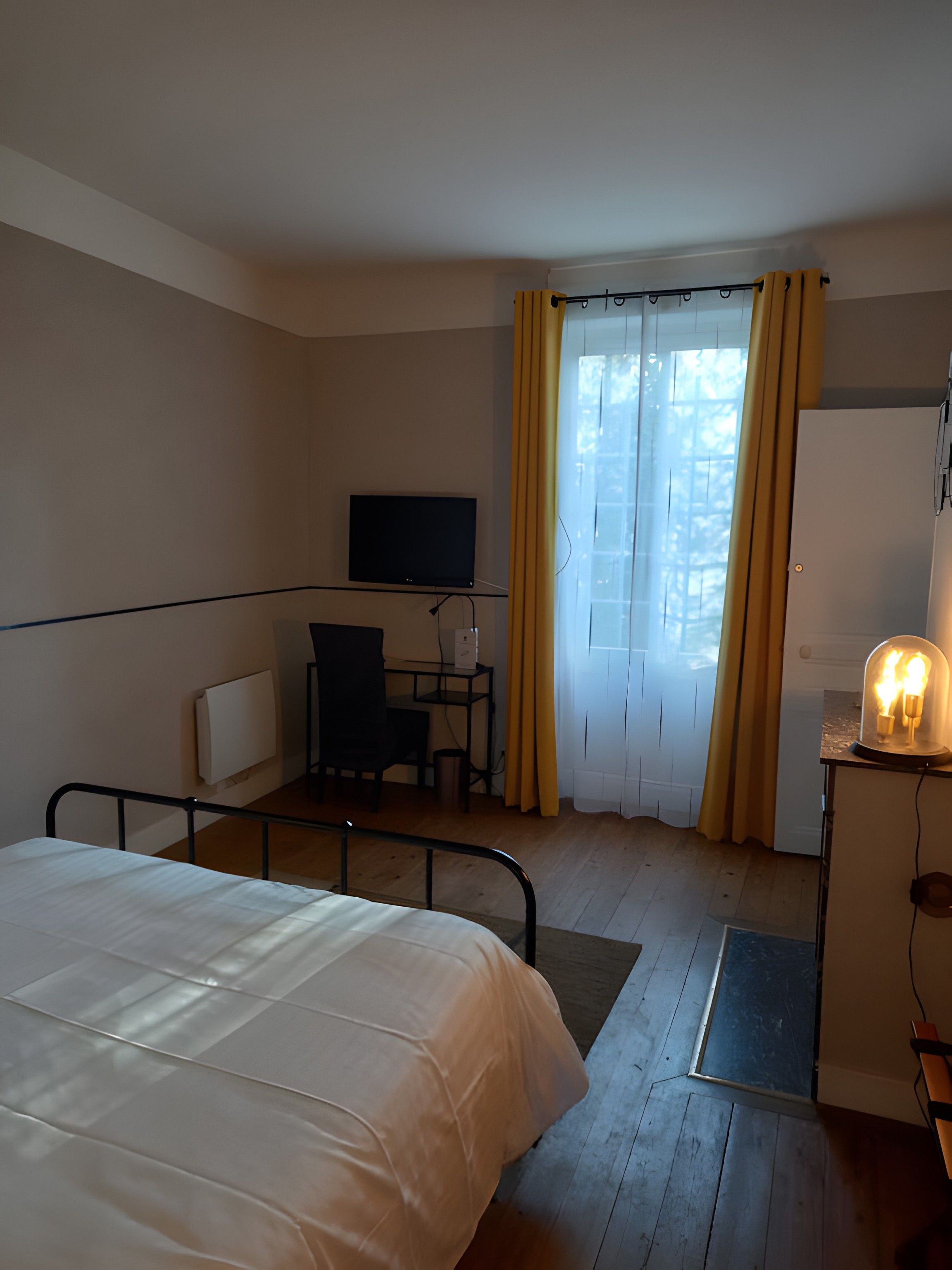 A hotel room with a bed, a desk, a chair, a television, and a window with curtains.