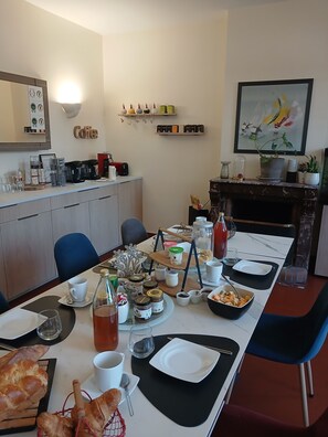 Un comedor con una mesa larga dispuesta para una comida, una estación de café con varios equipos para prepararlo y una chimenea con adornos.