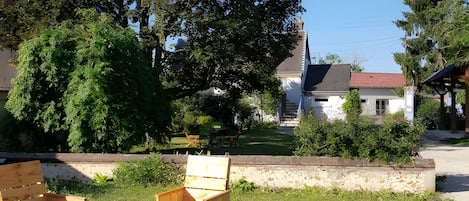 An outdoor seating area with wooden furniture, a stone wall, and a large tree in the background.