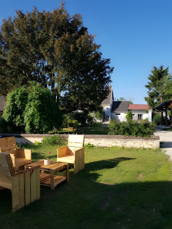 An outdoor seating area with wooden furniture, a stone wall, and a large tree in the background.
