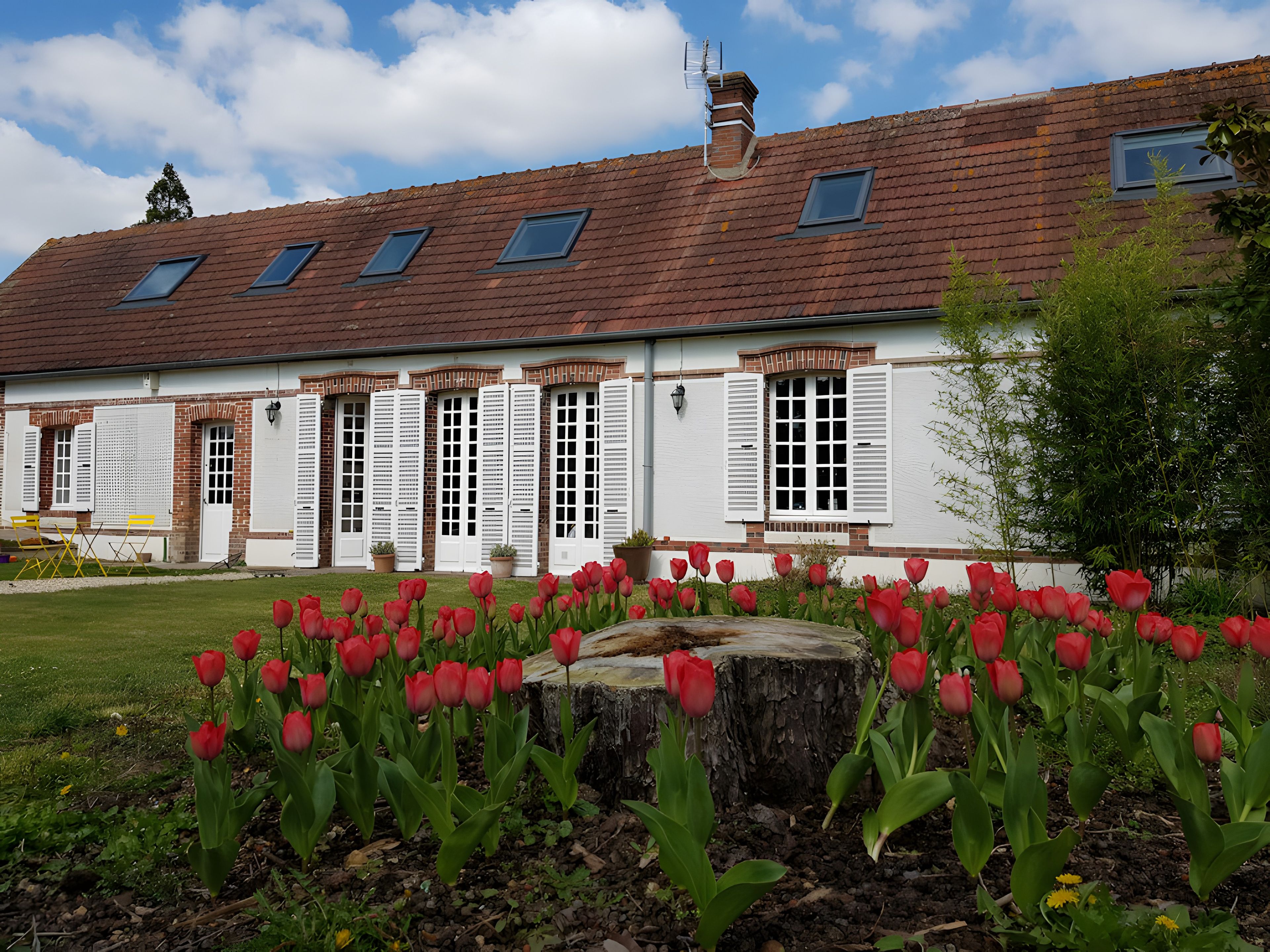A building with a sloped roof, multiple windows with shutters, and a garden with red tulips.
