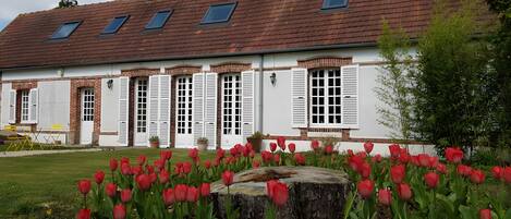 A building with a sloped roof, multiple windows with shutters, and a garden with red tulips.