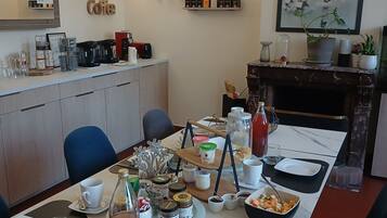 Een eetgedeelte met een lange tafel gedekt voor een maaltijd, een koffiehoek met diverse koffiezetapparaten, en een open haard met decoratieve objecten.