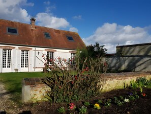 A building with a brick facade, multiple windows, and a garden area with various plants and flowers.