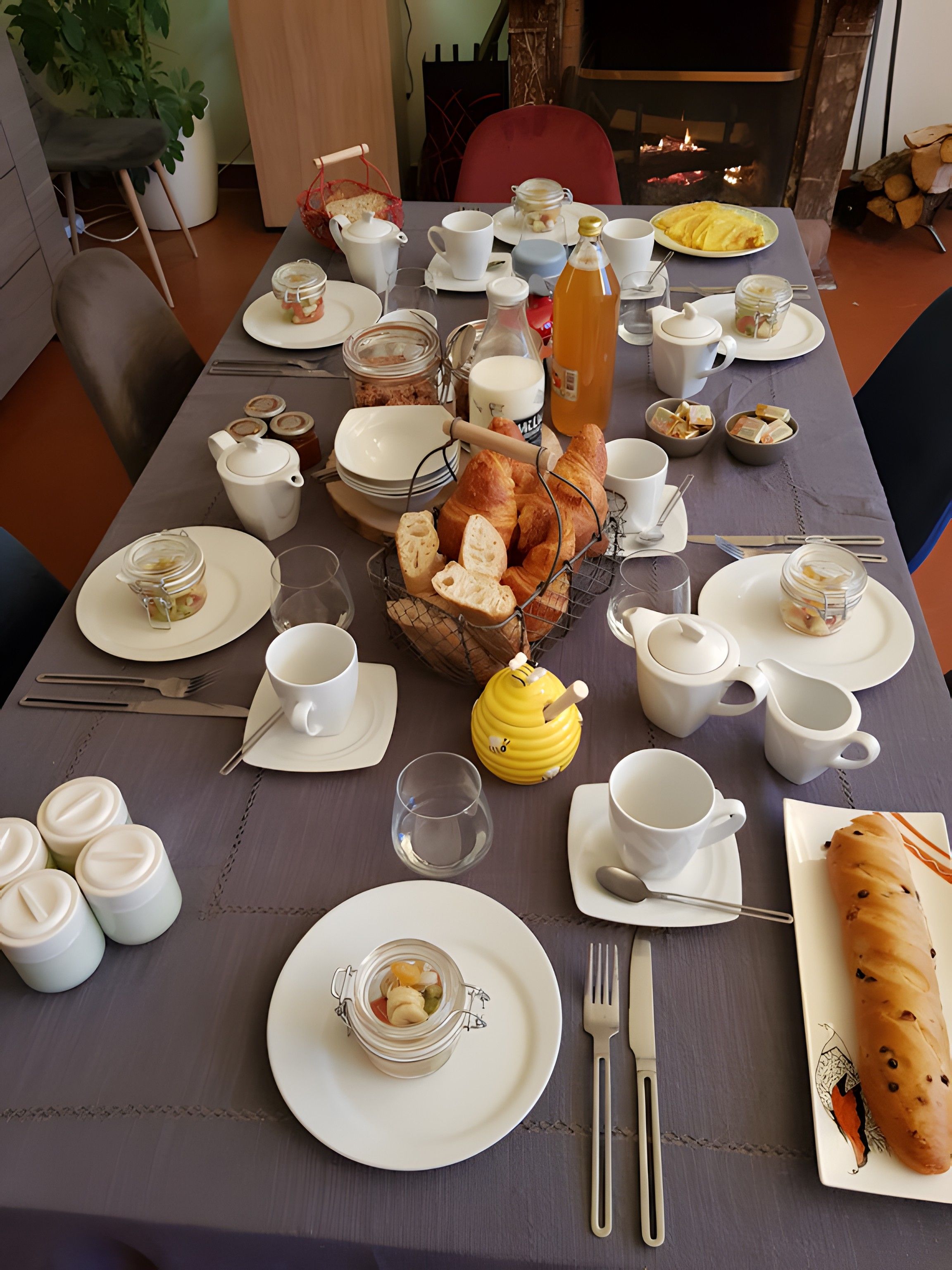 Een ontbijttafel gedekt met borden, bekers, een theepot, een karaf en een mand met brood.