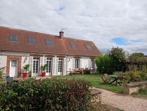 A two-story house with a tiled roof, multiple windows, and a garden area with outdoor furniture.
