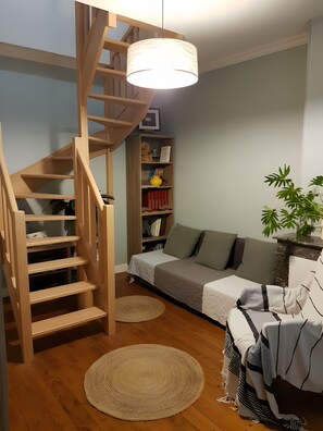 A room with a wooden staircase, a sofa, a bookshelf, and a hanging light fixture.