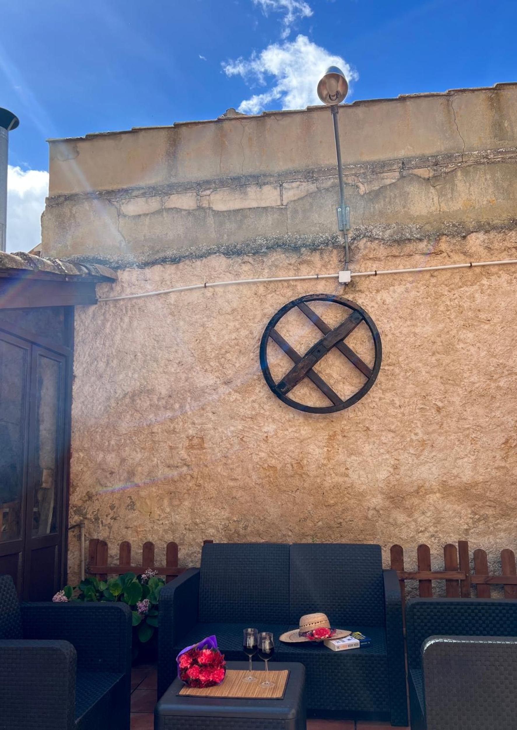 Een terras met rieten meubilair, een ronde metalen decoratie aan de muur en een houten omheining.