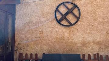 Een terras met rieten meubilair, een ronde metalen decoratie aan de muur en een houten omheining.