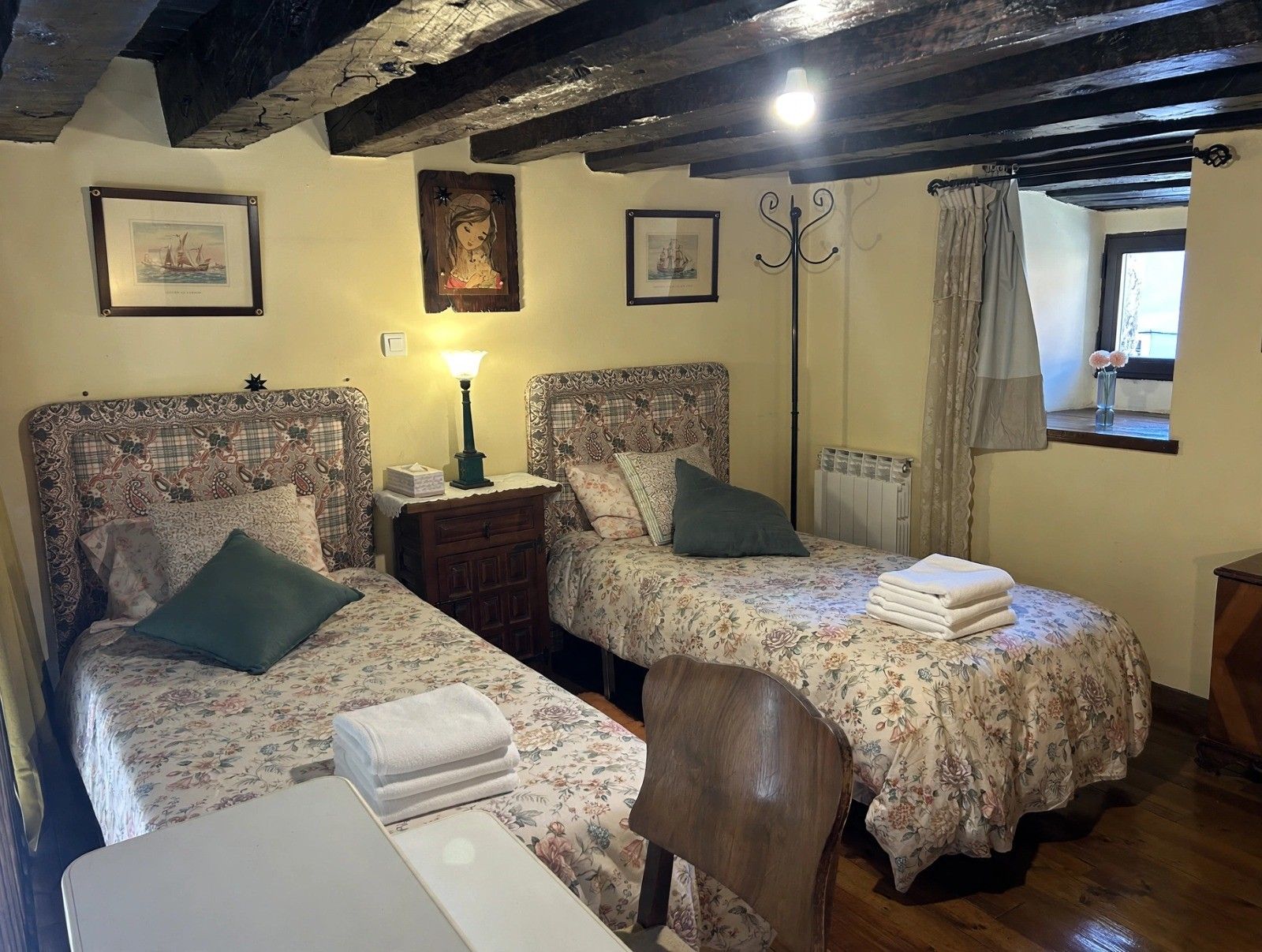 Una stanza con due letti, un comodino, una sedia e una finestra con tende.