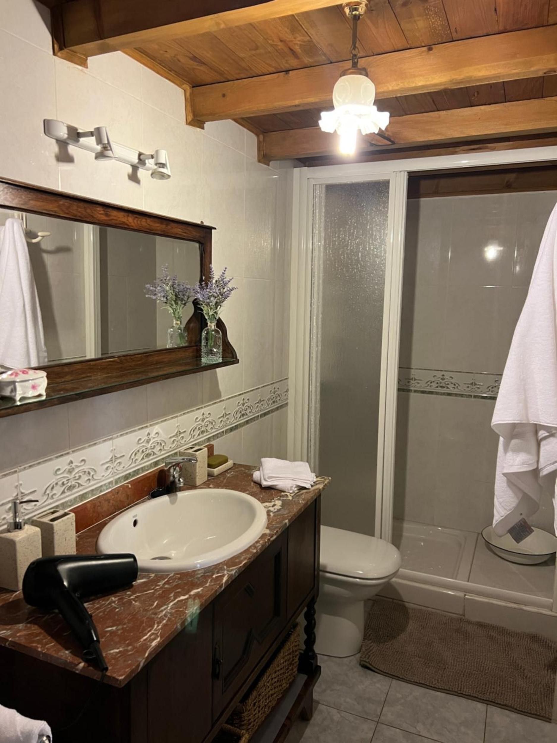 A bathroom with a marble sink, a mirror, a towel rack, a shower, and a wooden ceiling.