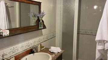 A bathroom with a marble sink, a mirror, a towel rack, a shower, and a wooden ceiling.