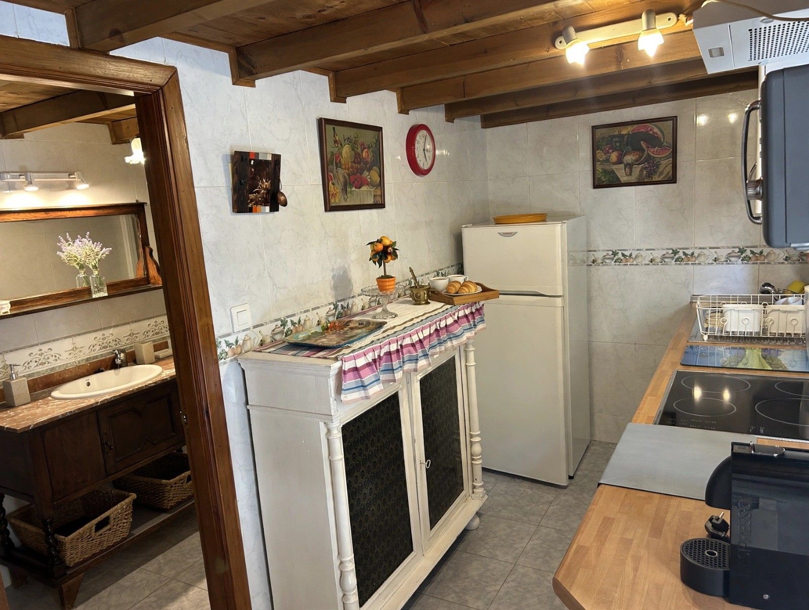 Una cocina con refrigerador, pileta y estufa. Hay objetos decorativos en la encimera y un reloj en la pared.