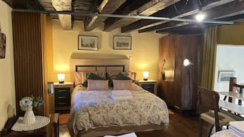 Une chambre avec un plafond en bois, un lit recouvert d’une literie à motifs floraux, des lampes de chevet et une armoire en bois.