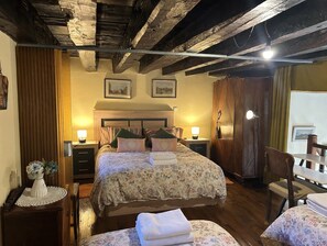 Quarto com teto de madeira, cama com roupa de cama florida, luminárias de cabeceira e guarda-roupa de madeira.