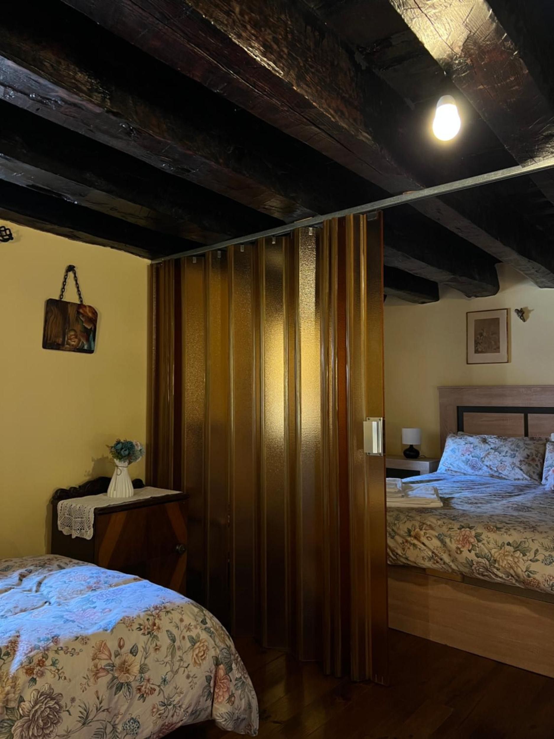 Una camera da letto con soffitto in legno, un letto con biancheria da letto a fiori, un comodino con una lampada e un quadro appeso al muro.