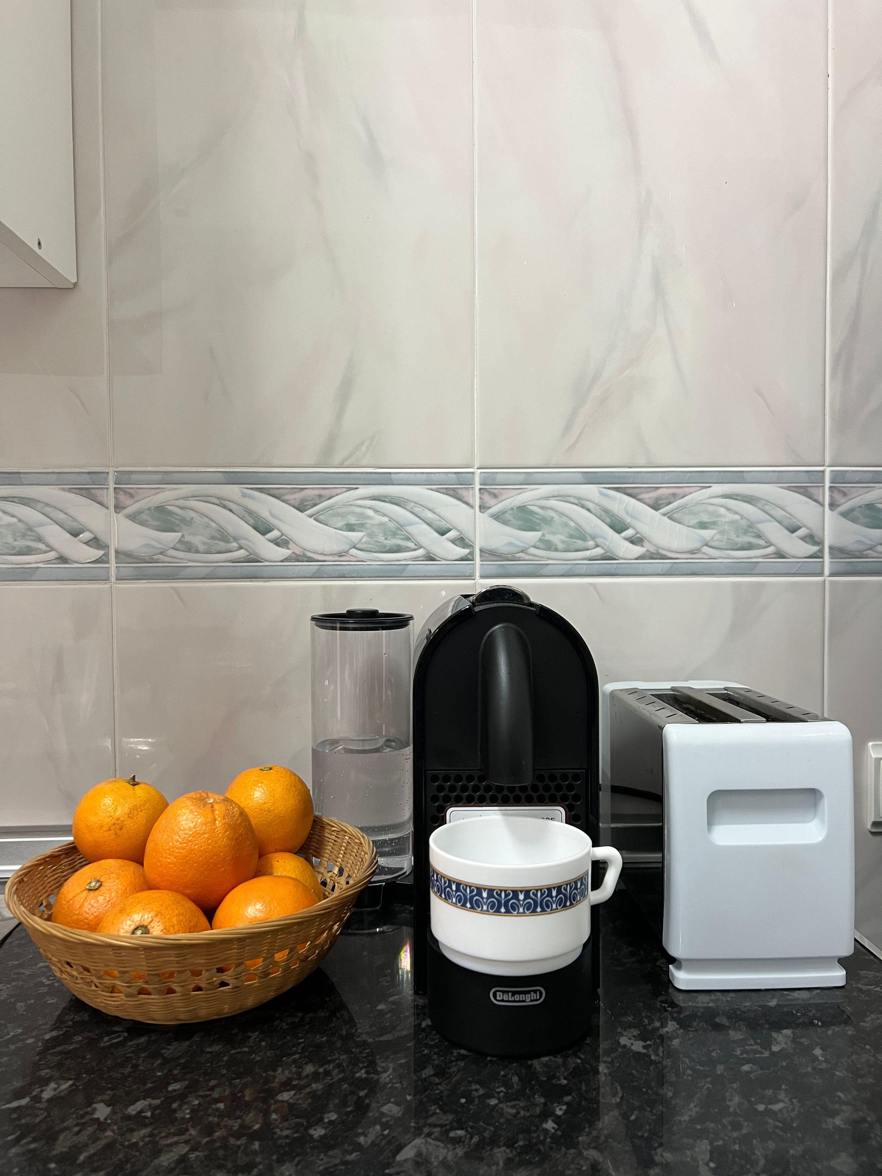 A kitchen counter with a basket of oranges, a coffee maker, and a toaster.