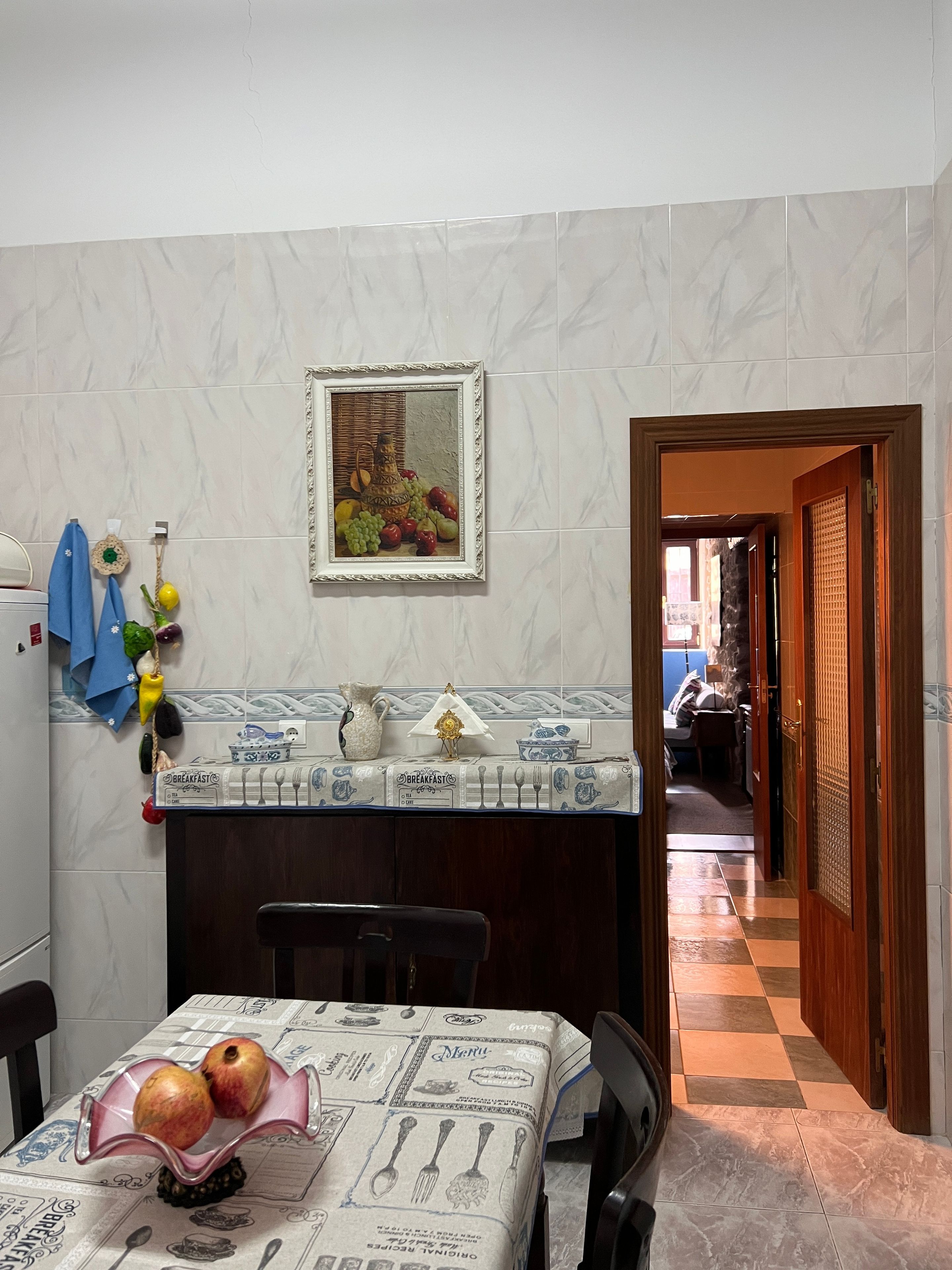 Une cuisine équipée d’une table à manger, d’un réfrigérateur, d’un évier et d’une porte-fenêtre donnant sur une autre pièce.