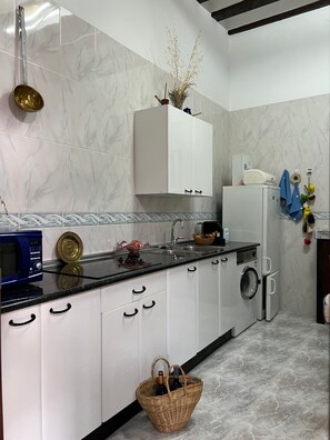 A modern kitchen with white cabinets, a microwave, a sink, and a washing machine.