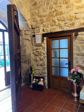 A stone wall, a wooden door with frosted glass panels, a metal bucket with flowers, and a metal bucket with umbrellas.