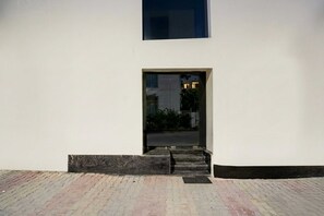 A building entrance with a glass door, a set of steps leading up to it, and a paved area in front. - Townhouse Railway Road Katra Formerly (Katra)