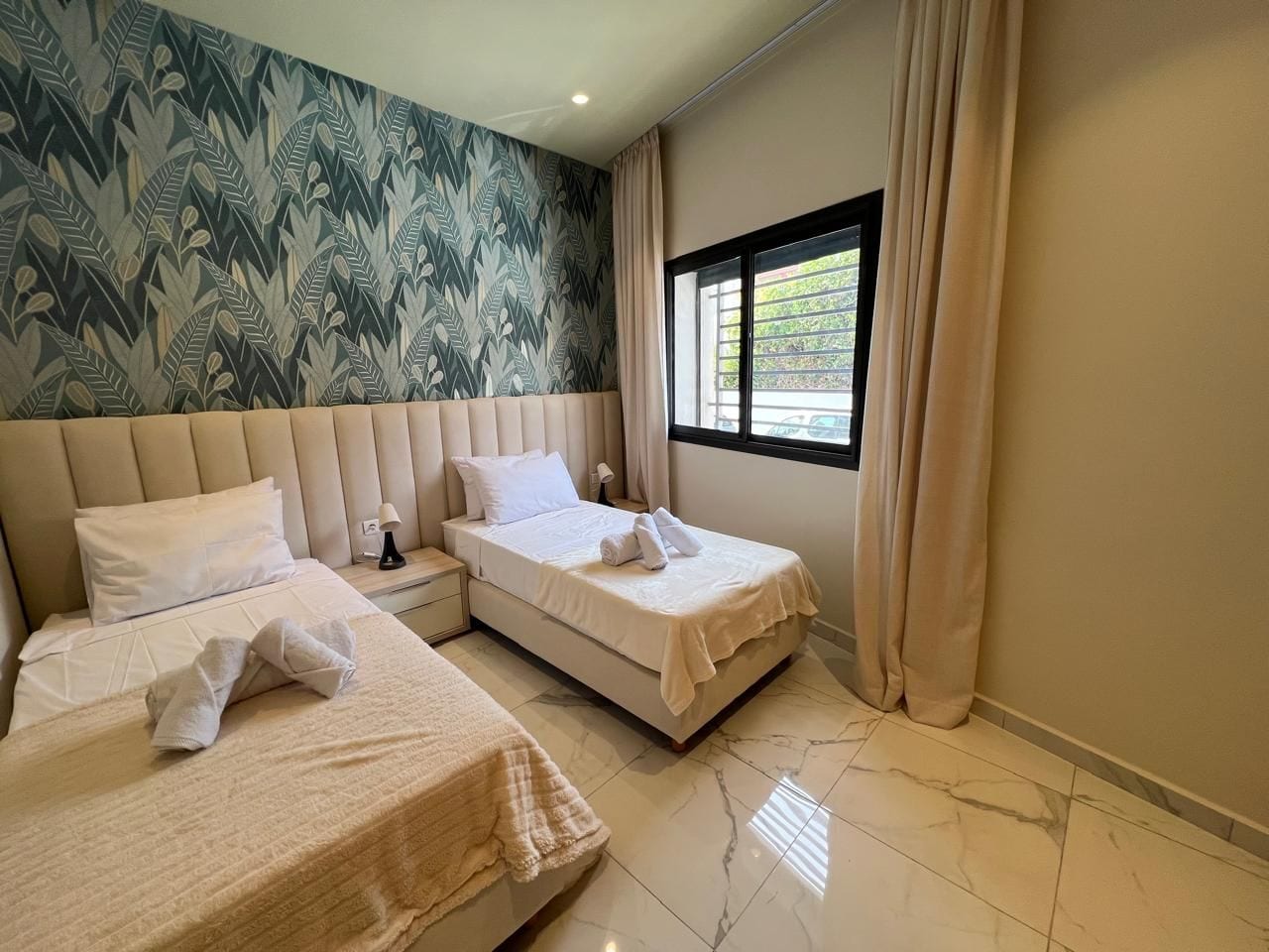 Une chambre d’hôtel avec deux lits, une grande fenêtre et un mur décoré d’un motif.