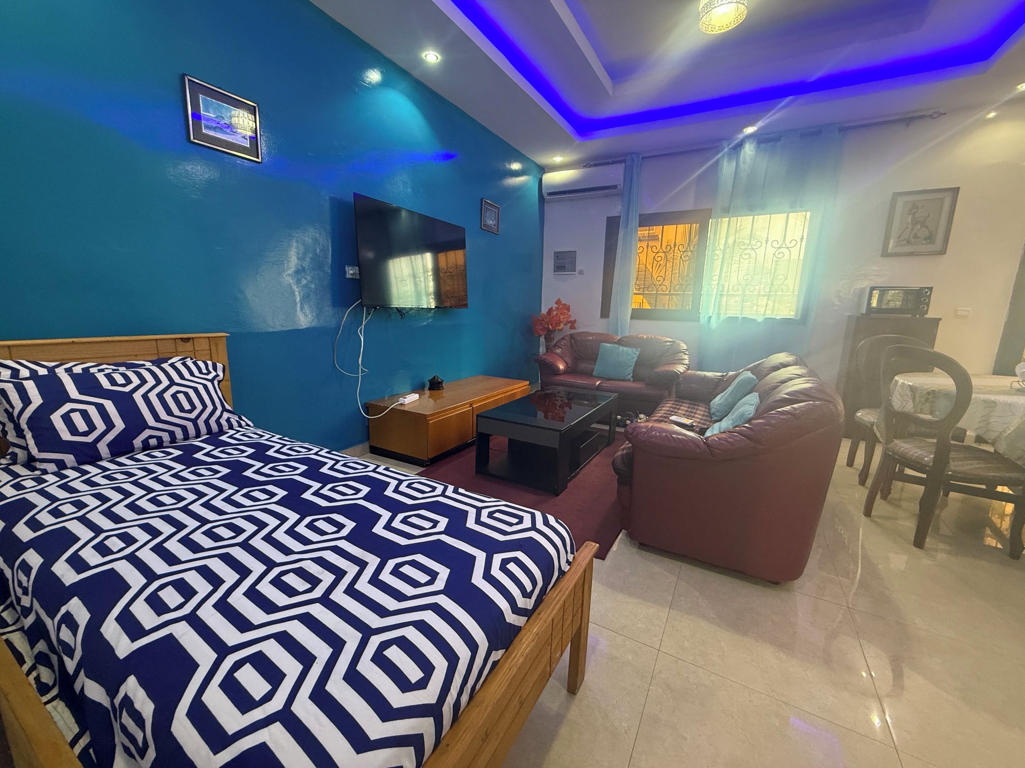 A room with a bed, a sofa, a coffee table, a TV, and a dining area.