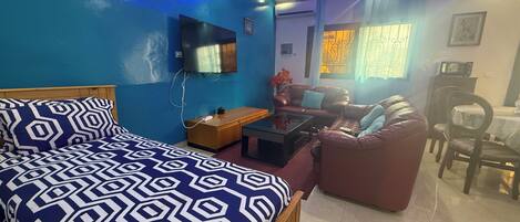A room with a bed, a sofa, a coffee table, a TV, and a dining area.