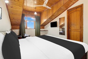 A hotel room with a large bed, wooden ceiling, a ceiling fan, a window with curtains, a flat-screen TV, and a wooden door. - Super Townhouse Rajbagh Formerly Hotel (Srinagar)