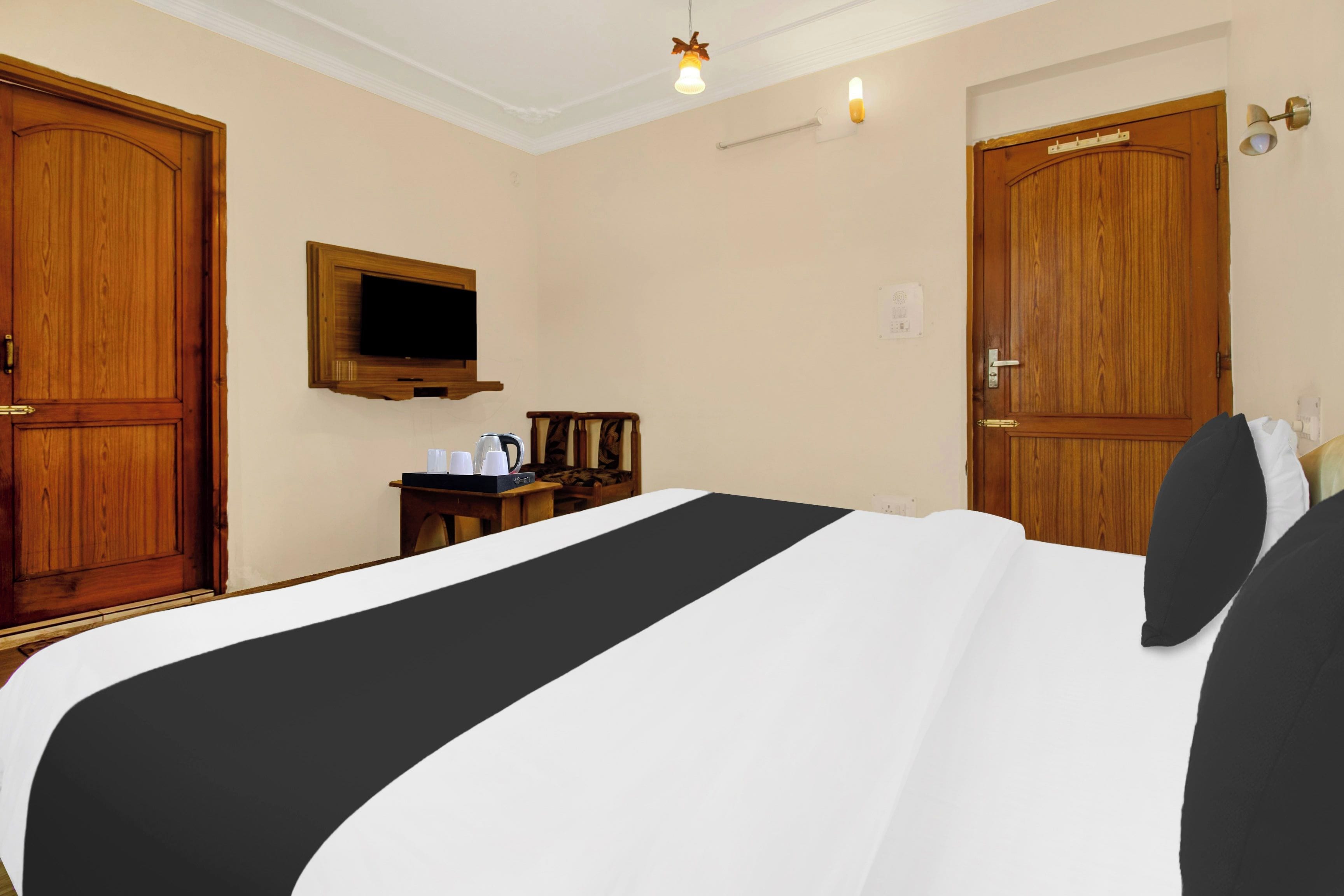 Quarto de hotel com uma cama grande, guarda-roupa de madeira, televisão na parede e uma pequena mesa com chaleira e chávenas.