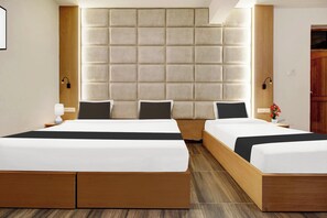 Habitación de hotel con dos camas, un cabecero grande y acolchado, lámparas de noche y suelo de madera.