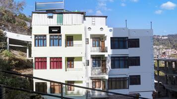 A multi-story building with balconies and windows, situated on a hillside.