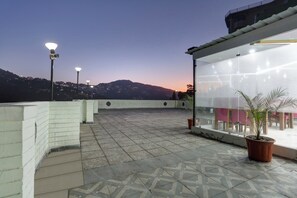 A rooftop terrace with patterned tiles, a glass enclosure with a view, and street lamps. - Townhouse Kachighati Formerly Palm Bliss (Shimla)