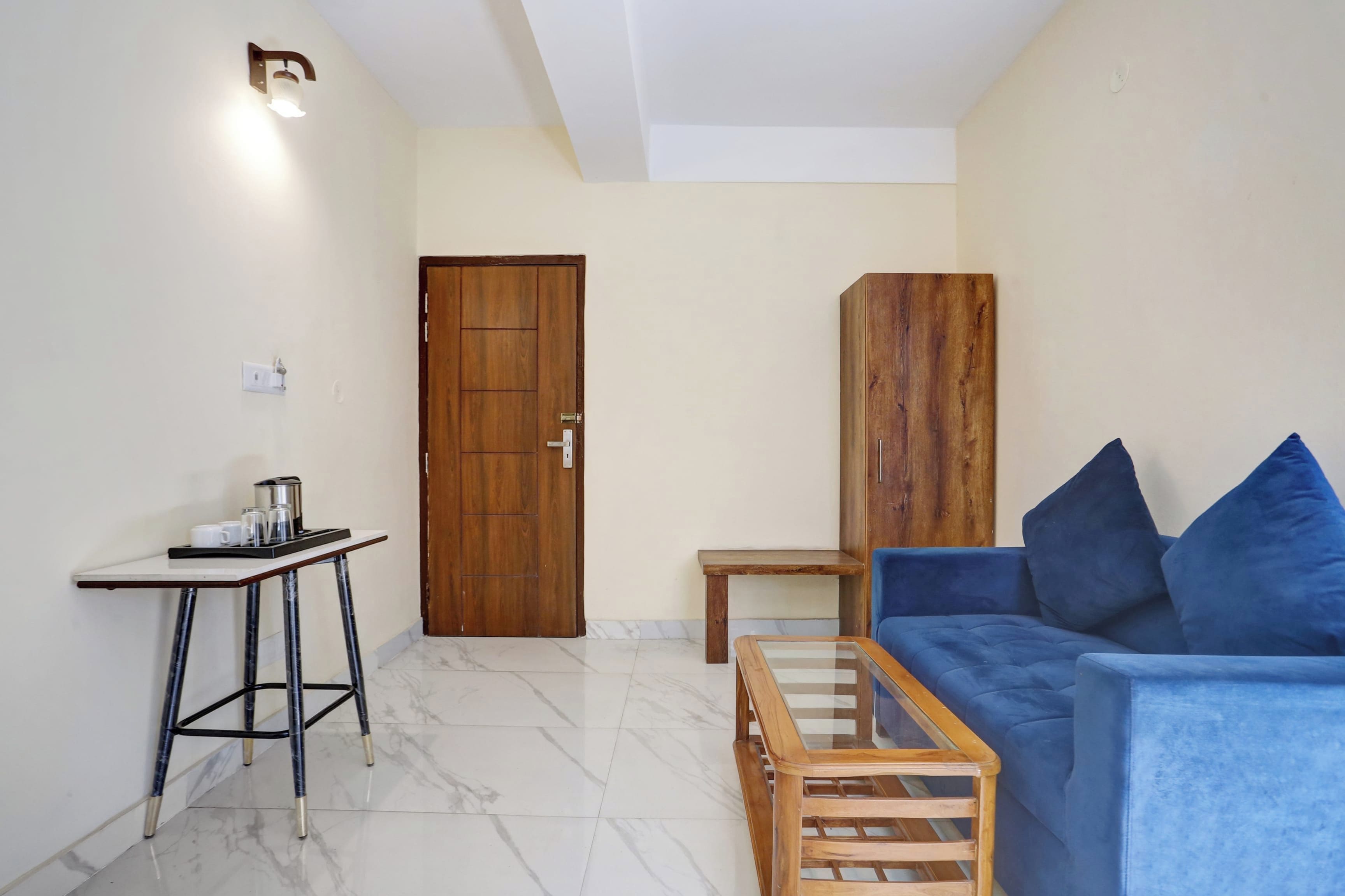 Um espaço de estar compacto com porta de madeira, uma mesa pequena, sofá com almofadas azuis e piso de mármore.