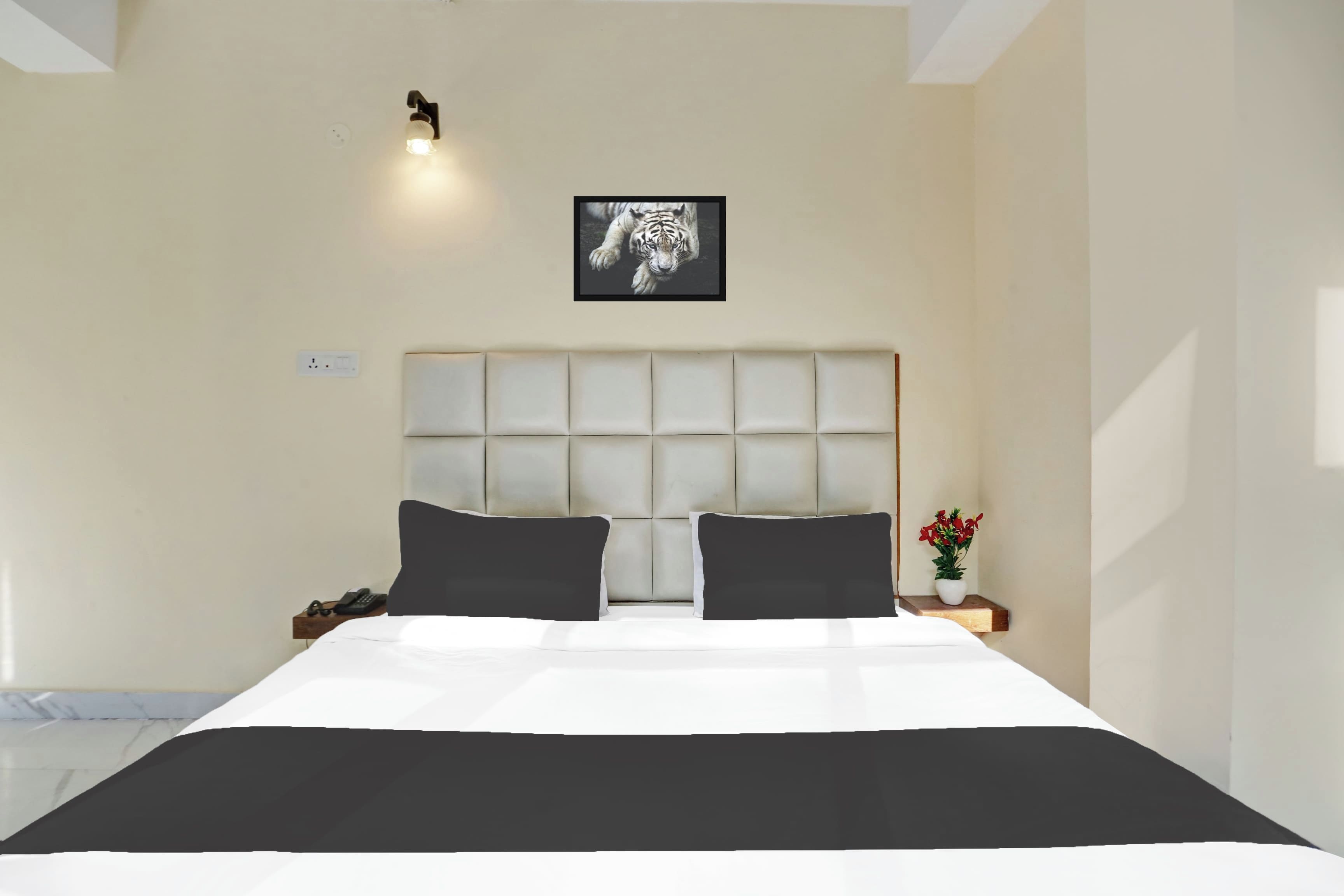 Un dormitorio con una cama grande, cabecera, dos mesitas de noche, una lámpara de pared e imagen enmarcada sobre la cama.