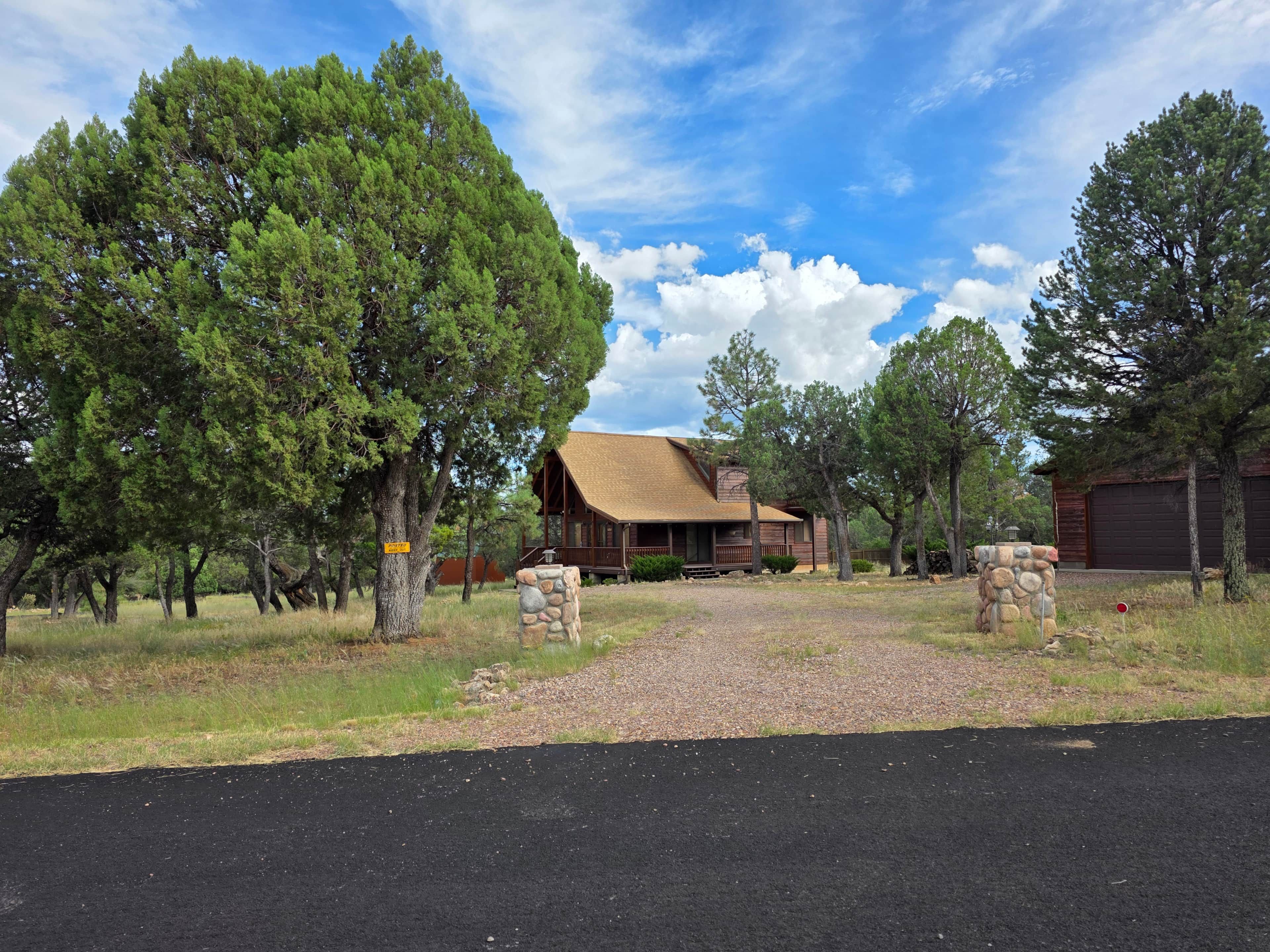 Una cabaña rústica con una estructura de madera destacada, rodeada por un paisaje natural con árboles y un cielo despejado.