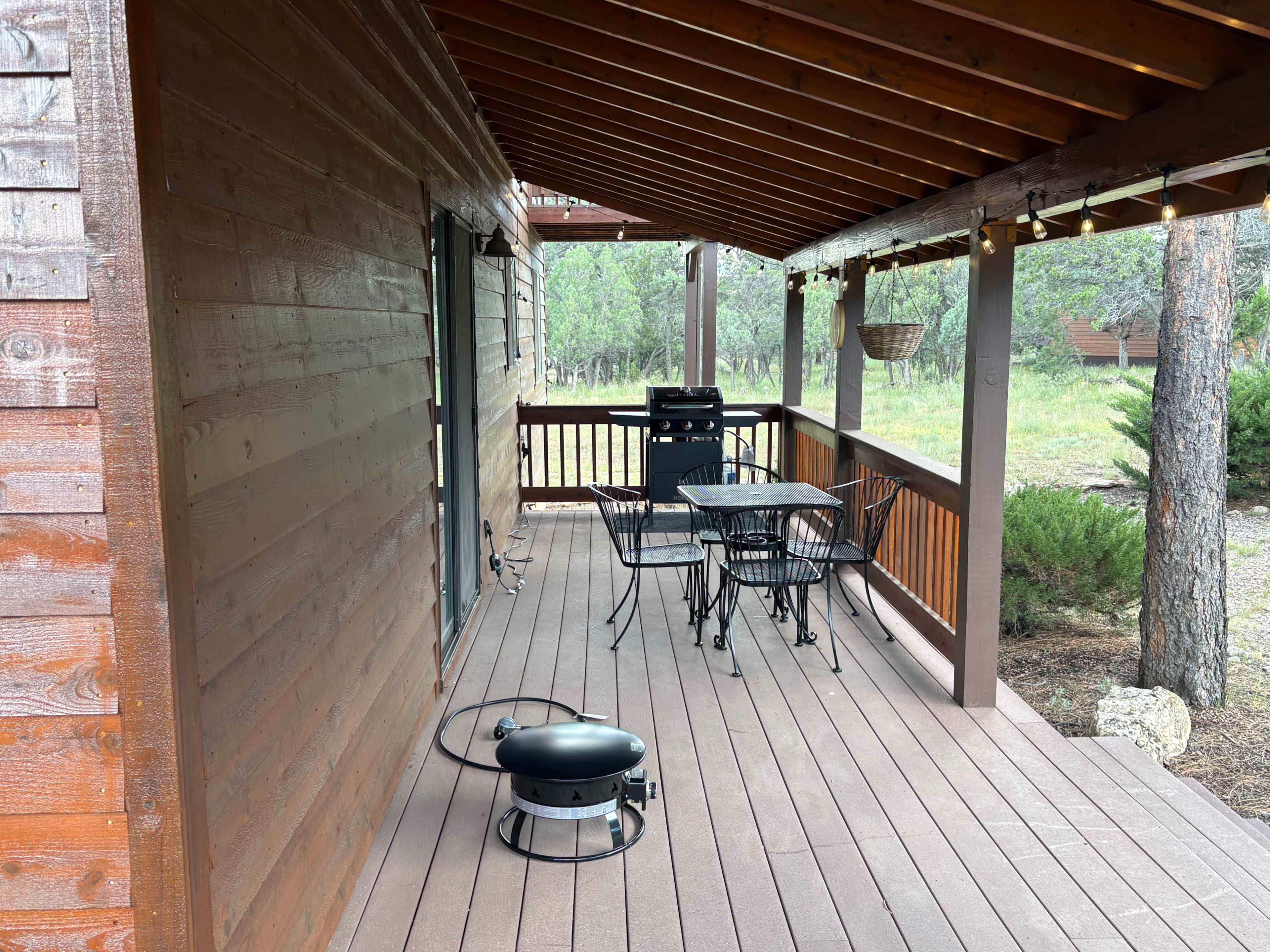 Una terraza techada al aire libre con una parrilla, sillas de metal y una mesa.