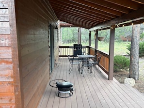 A covered outdoor deck with a grill, metal chairs, and a table. - Elk Springs Cabin (Overgaard)