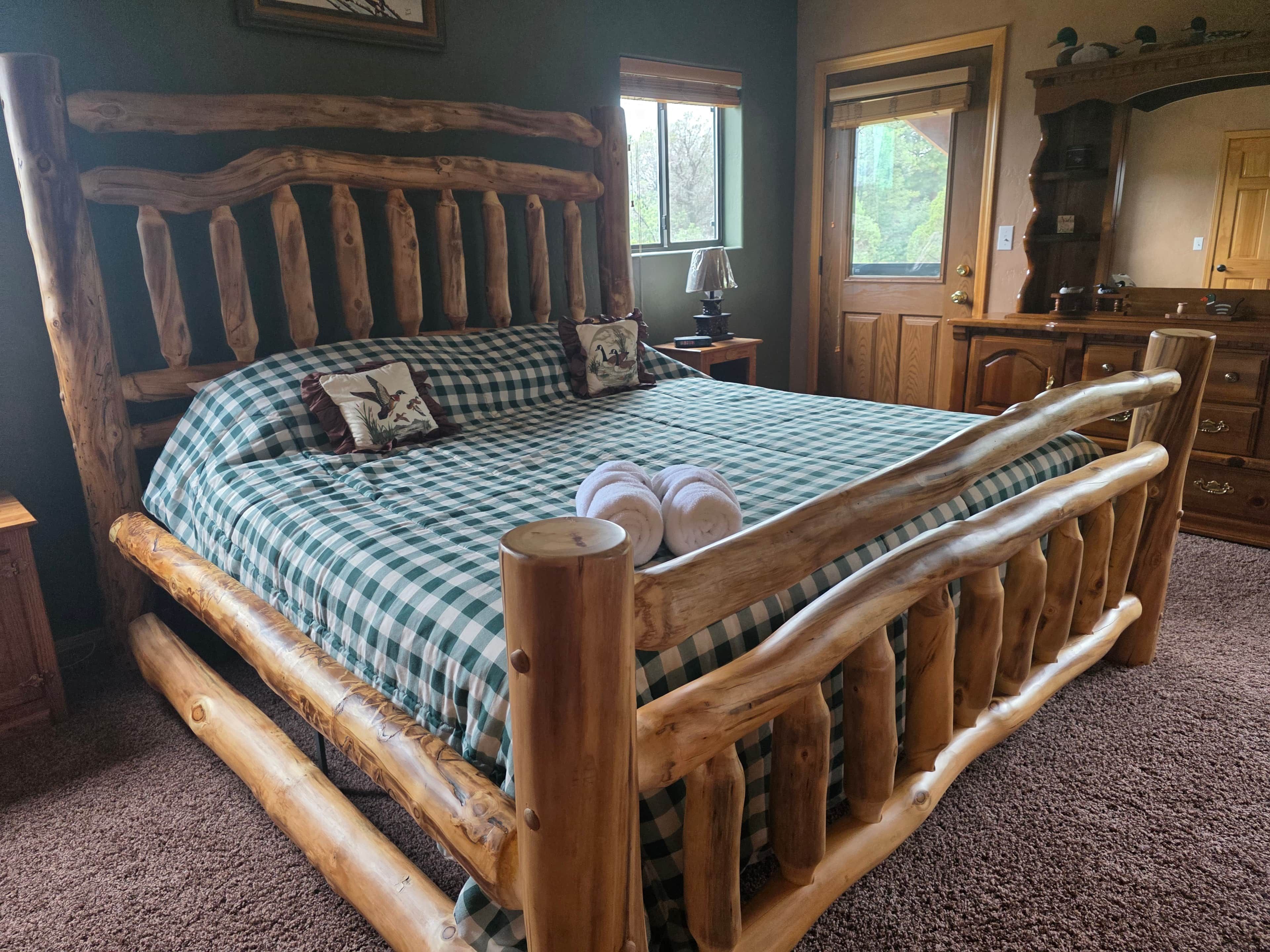 Una cama de madera con colcha a cuadros y almohadas, cabecero de madera y una mesita de noche con lámpara.