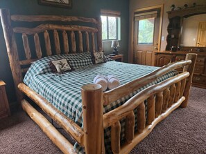 A wooden bed with a checkered bedspread and pillows, a wooden headboard, and a small bedside table with a lamp. - Elk Springs Cabin (Overgaard)