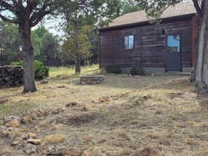 A rustic wooden cabin with a stone fire pit, surrounded by dry grass and trees. - Elk Springs Cabin (Overgaard)