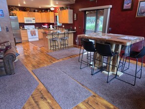 A kitchen with wooden cabinets, a microwave, and a stove. There is a dining area with a table and chairs. - Elk Springs Cabin (Overgaard)