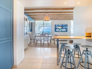 A modern kitchen with a dining area, wooden ceiling beams, and a TV displaying a menu.