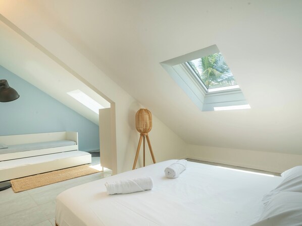 A bedroom with a skylight, a bed with white linens, a bedside table, and a chair.