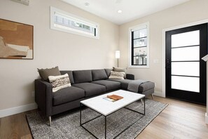 Ein modernes Wohnzimmer mit einer Eckcouch, einem Couchtisch und einem großen Fenster, das für natürliches Licht sorgt.