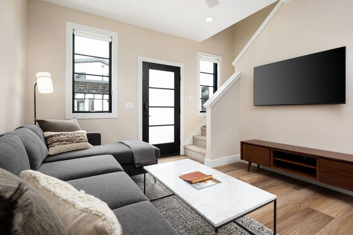 Una sala de estar moderna con un sofá modular, una mesa de centro, un televisor de pantalla plana y una escalera.