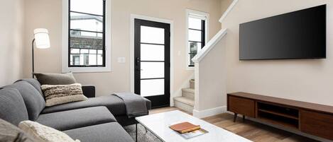 Una sala de estar moderna con un sofá modular, una mesa de centro, un televisor de pantalla plana y una escalera.